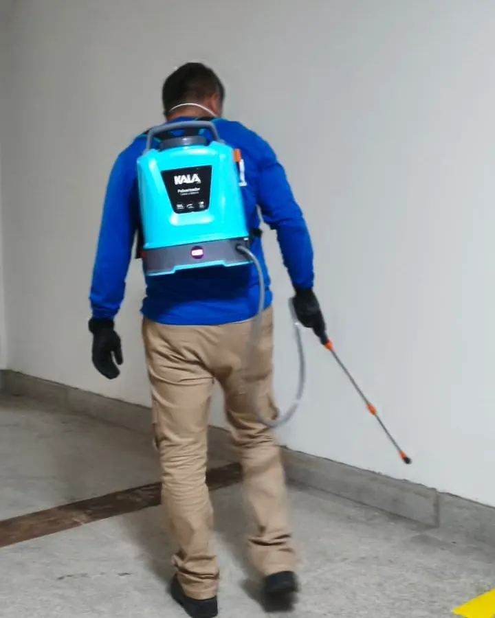 Profissional com pulverizador costal aplicando controle de pragas em corredor